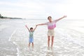 Asian mother and little boy standing at tropical sand beach with waving hands and open wide. Happy family mom and son having fun Royalty Free Stock Photo