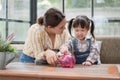 Asian mother and little daughter putting coins into piggy bank Royalty Free Stock Photo