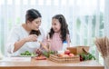 Asian mother and little helper, Caucasian child daughter preparing breakfast in kitchen, mixing vegetables and fruit in salad bowl Royalty Free Stock Photo