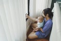Asian mother and newborn baby boy sitting on floor doing online video call with family on smartphone at home
