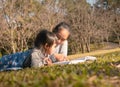 Asian mother reading a book to her daughter in spring garden. Family spending time together on picnic on summer vacation Royalty Free Stock Photo