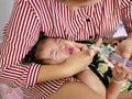 Asian mother`s arm wrapping around her crying baby girl`s face forcing the baby to take liquid medicine Royalty Free Stock Photo