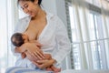 Asian mother with smiling give breastfeeding newborn with white shirt and sitting on bed white background of glass windows and