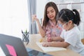 Asian mother teaching baby girl wearing eyeglasses doing home using laptop and write notes in notebook to study online on wood Royalty Free Stock Photo