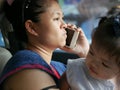 Asian mother uncomfortably making a phone call while dealing with her daughter in a driving car