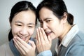 Asian mother whispering gossiping in her daughter ear,adult woman look at other with disdain,aversion,telling a secret to Royalty Free Stock Photo