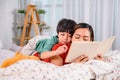 Asian mother work home together with son. Mom and kid reading fairy tale before sleep on the bed. Woman lifestyle and family Royalty Free Stock Photo