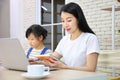 Asian mother working online from home using laptop while watching her daughter working on assignment from school for homeschooling Royalty Free Stock Photo