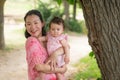 Asian mum and little child - young happy and beautiful Korean woman playing on city park with adorable and cheerful baby girl in Royalty Free Stock Photo