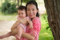 Asian mum and little child - young happy and beautiful Korean woman playing on city park with adorable and cheerful baby girl in Royalty Free Stock Photo