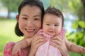 Asian mum and little child - young happy and beautiful Korean woman playing on city park with adorable and cheerful baby girl in Royalty Free Stock Photo