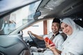 Asian Muslim couple smiles while using cell phone in car