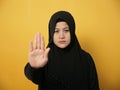 Asian muslim lady wearing hijab shows stop sign, prohibit forbid disallow something bad with palm hand gesture, against yellow Royalty Free Stock Photo