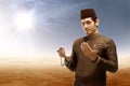 Asian muslim man standing and praying while raised arms with prayer beads on desert Royalty Free Stock Photo