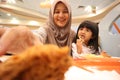 Asian muslim mother and baby girl daughter eating at fast food restaurant, family enjoys fried chicken, burger and potato chips Royalty Free Stock Photo