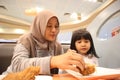 Asian muslim mother and baby girl daughter eating at fast food restaurant, family enjoys fried chicken, burger and potato chips Royalty Free Stock Photo