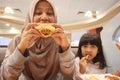 Asian muslim mother and baby girl daughter eating at fast food restaurant, family enjoys fried chicken, burger and potato chips Royalty Free Stock Photo