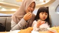 Asian muslim mother and baby girl daughter eating at fast food restaurant, family enjoys fried chicken, burger and potato chips Royalty Free Stock Photo