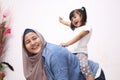 Asian muslim mother playing with her little baby girl daughter sit on her back, acting like a horse for her kid, happy smiling Royalty Free Stock Photo