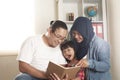 Asian muslim parent, mother, father and child are reading a book at home, happy excited expression