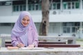 Asian Muslim university student doing homework alone outdoors on campus.