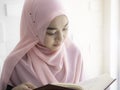 An Asian Muslim woman is concentrating on reading the Al Quran, concentrating carefully in the mosque with the warm sunlight Royalty Free Stock Photo