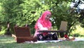 Asian muslim woman with hijab sit in park working or online communication with friends or family by using laptop, relaxing freelan