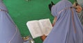 Asian muslim woman is reading sholawat from a book