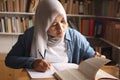 Asian muslim woman studying in library, exam preparation concept. Female college student doing research and making notes in her Royalty Free Stock Photo