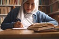 Asian muslim woman studying in library, exam preparation concept. Female college student doing research and making notes in her Royalty Free Stock Photo