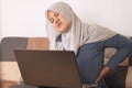 Asian muslim woman typing on laptop at home and having back pain, neck muscle pain tension, too much using computer Royalty Free Stock Photo