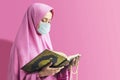 Asian Muslim woman in a veil and wearing flu mask holding prayer beads and reading the Quran Royalty Free Stock Photo