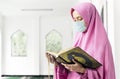 Asian Muslim woman in a veil and wearing flu mask holding prayer beads and reading the Quran Royalty Free Stock Photo