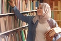 Asian muslim woman wearing hijab picking book in bookshelf, education concept, reading learning studying in library Royalty Free Stock Photo