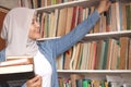 Asian muslim woman wearing hijab picking book in bookshelf, education concept, reading learning studying in library Royalty Free Stock Photo