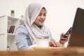 Asian muslim woman work in office, using phone and laptop, happy smiling facial expression, online shopping check out Royalty Free Stock Photo