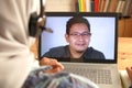 Asian muslim woman having video teleconference witha man on her laptop at home, online learning or working from home