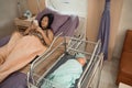 Baby laying in crib with his mother using mobile phone laying on bed side Royalty Free Stock Photo