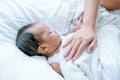 Asian newborn baby is sleeping on white bed with mother hand put on her chest to take care and make her feel safe
