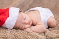 Asian newborn baby wearing christmas hat sleeping on brown blanket, adorable infant lying on bed at home with trust and safe. Royalty Free Stock Photo