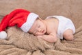 Asian newborn baby wearing christmas hat sleeping on brown blanket, adorable infant lying on bed at home with trust and safe. Royalty Free Stock Photo