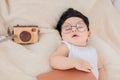 Asian Newborn baby wearing glasses with favorite book on beige blanket , 3 month-old infant lying in bed with relax. Adorable baby Royalty Free Stock Photo