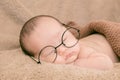 Asian Newborn baby wearing glasses and sleep on brown bed at home, 0-1month-old infant lying in blanket with relax. Adorable baby