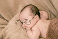 Asian Newborn baby wearing glasses and sleep on brown bed at home, 0-1month-old infant lying in blanket with relax. Adorable baby