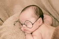 Asian Newborn baby wearing glasses and sleep on brown bed at home, 0-1month-old infant lying in blanket with relax. Adorable baby