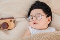 Asian Newborn baby wearing glasses sleeping with beige blanket next to toy camera with safe and comfortable. Adorable baby resting