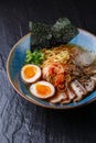 Asian noodle soup, ramen with pork, tofu, kimchi, vegetables and egg in blue bowl. Slate background. Top view. Bowl of Royalty Free Stock Photo