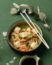 Asian noodles or spaghetti with shrimp, vegetables and sesame seeds. Bowl and chopstick on green background. Pan-Asian