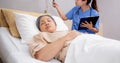 Asian nurse check saline and check patient elderly while asleep on bed at hospital ward.