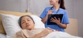 Asian nurse check saline and check patient elderly while asleep on bed at hospital ward.